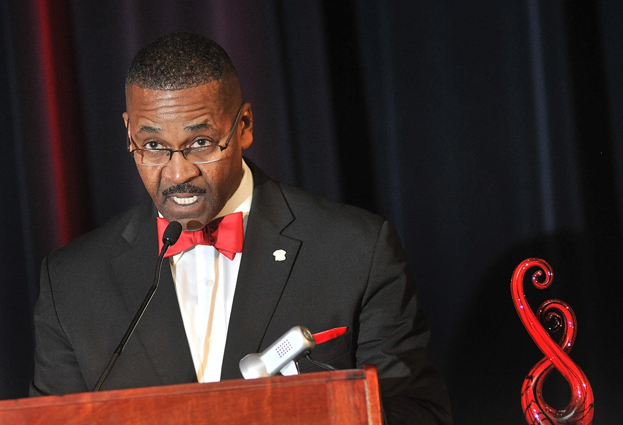 Rev. John Moore speaking at a podium in a red bow tie